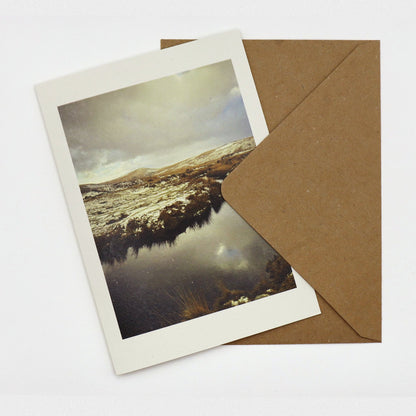 Snow at Taw Marsh Christmas card showing snowy Dartmoor hills reflected in dark water, with kraft envelope