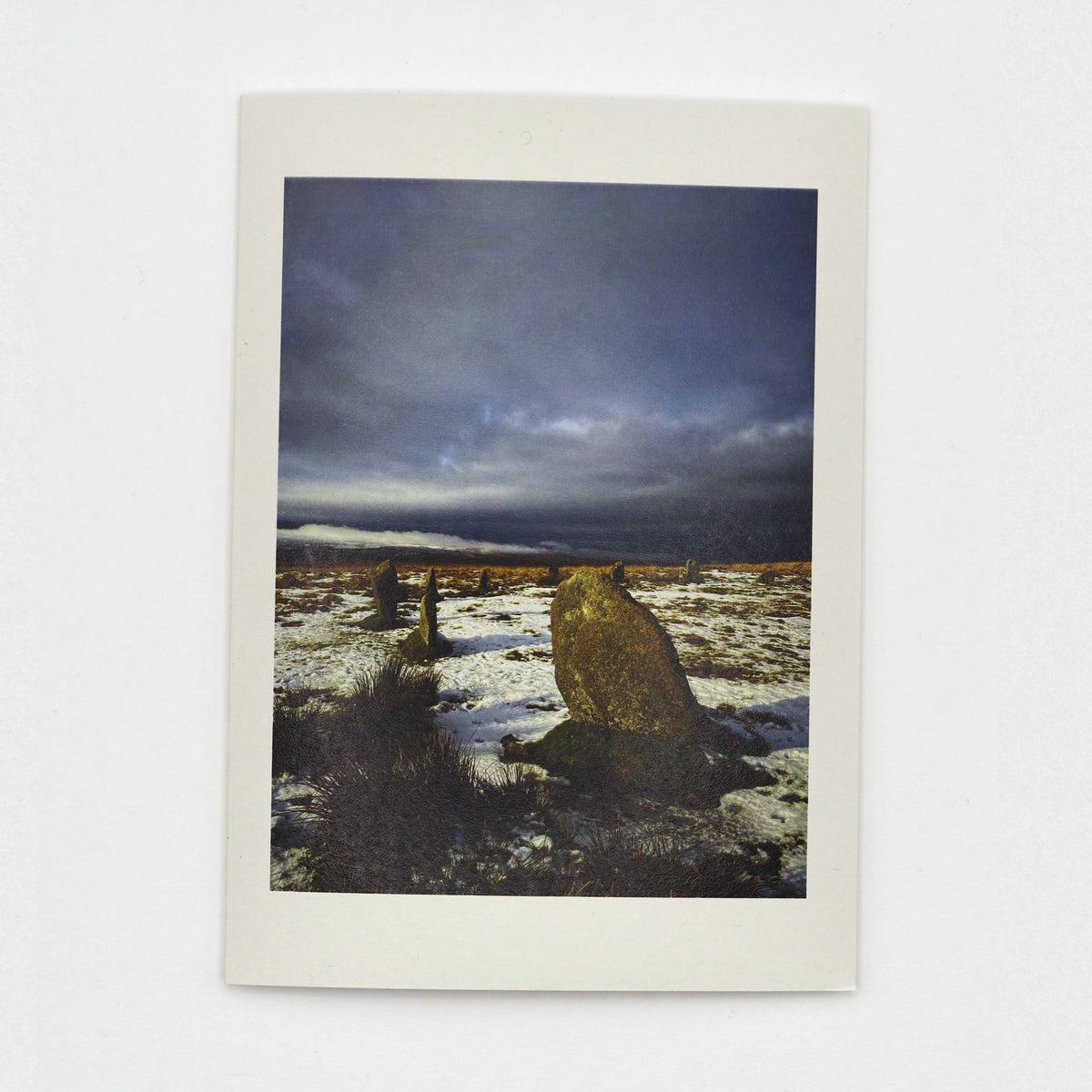 Snow at the Stones Christmas card showing Whitmoor ancient stone circle  in snow on Dartmoor under a dark stormy sky