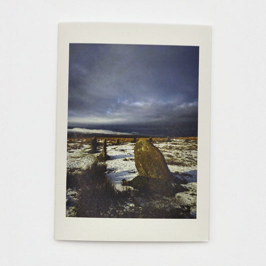 Snow at the Stones Christmas card showing Whitmoor ancient stone circle  in snow on Dartmoor under a dark stormy sky