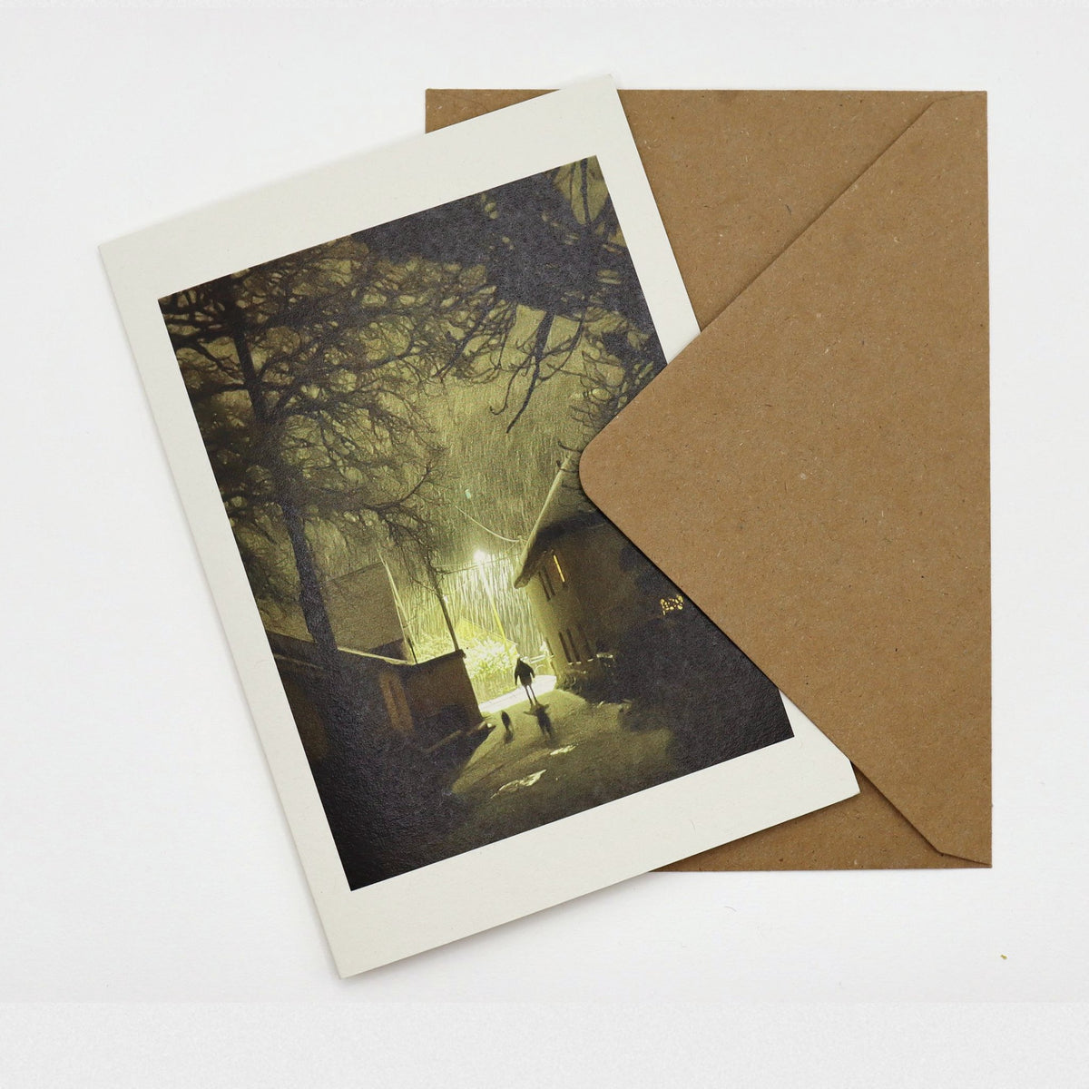 Sticklepath Snow Christmas card showing snow falling at night under a street lamp, a figure and two dogs in the lane