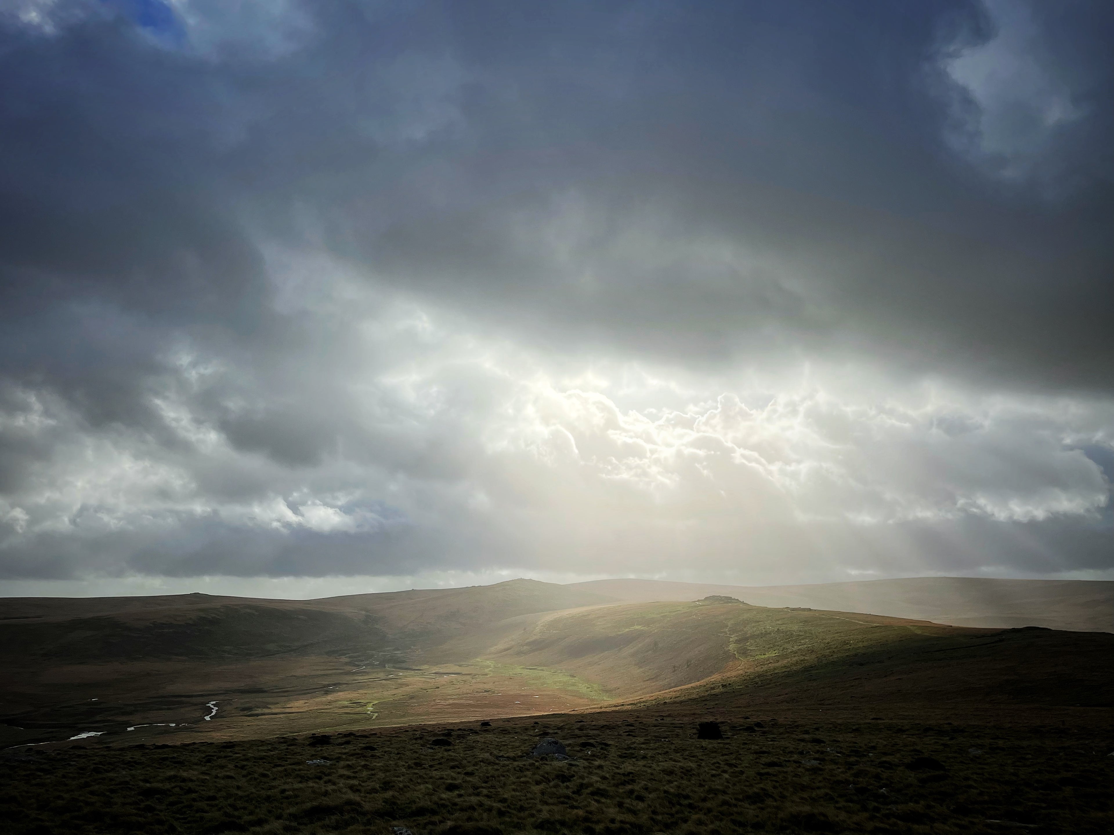 Sunlight breaking through dark clouds over a hilly landscape